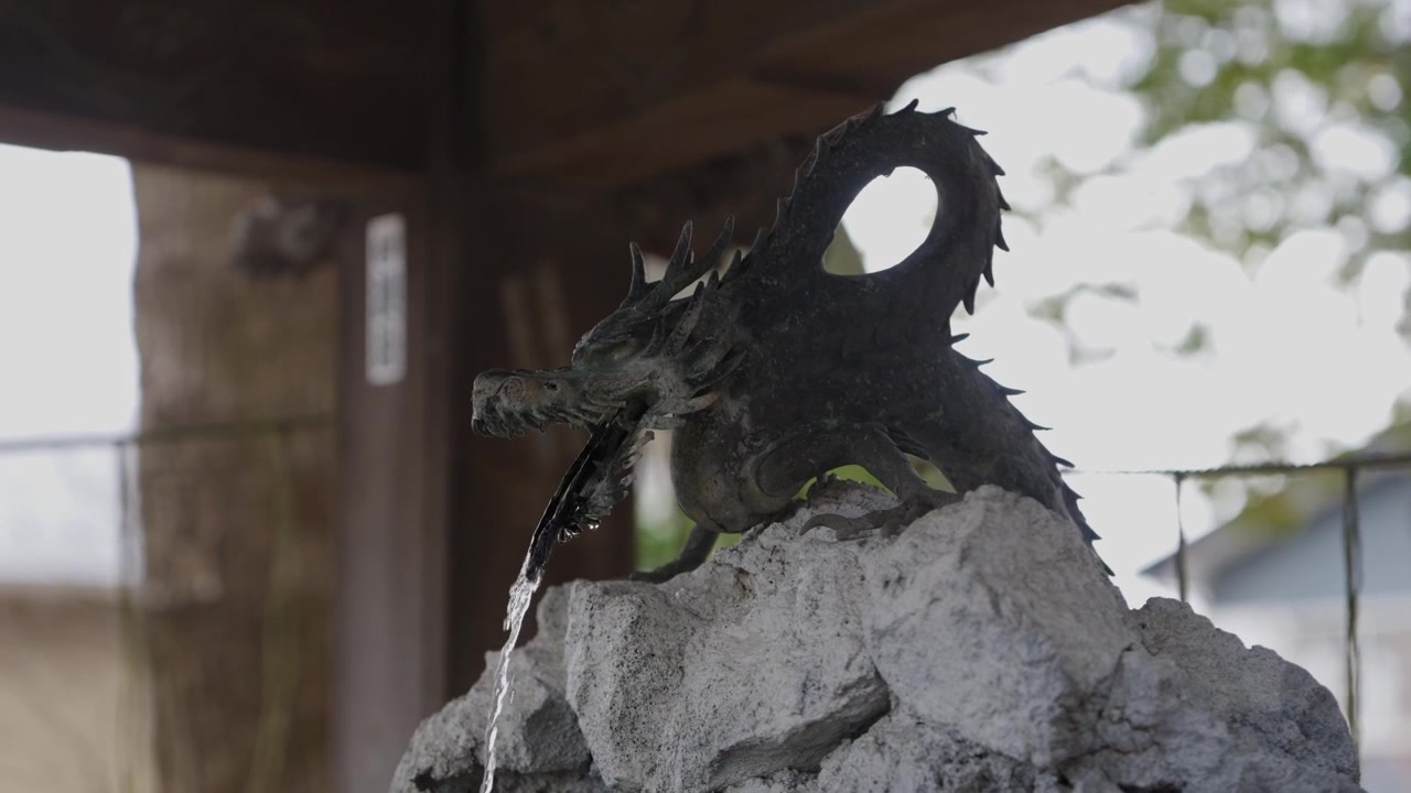Bronze dragon fountain pouring water over stone at a Shinto shrine purification basin in Japan