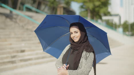 young muslim woman in hijab hiding under umbrella on sunny day.