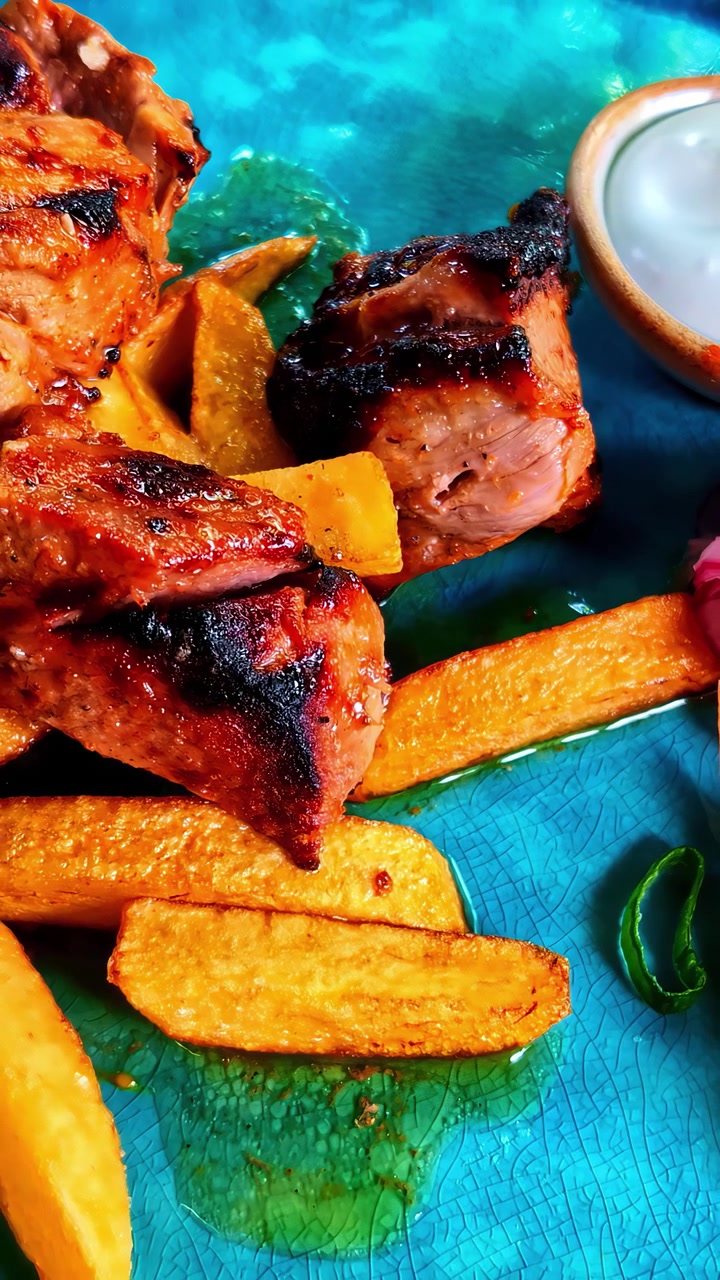 Primo piano di carne alla griglia con patatine fritte croccanti su un piatto blu, accompagnata da una salsa d'accompagnamento. Adatto per blog culinari o promozioni alimentari.