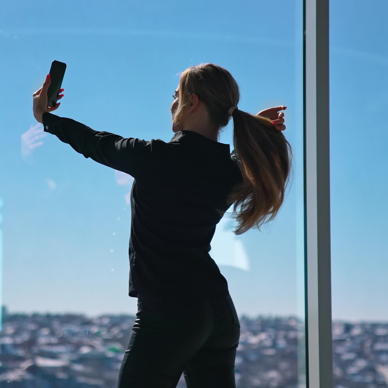 Beautiful girl doing selfie near the on window. Young business woman taking photos of herself on mobile phone in office