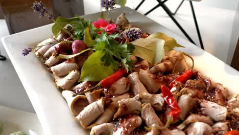 platter with deli meat in sauce, accompanied by chili peppers, grapes, and herbs