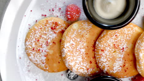 ukrainian cheese pancakes presenting golden brown texture, garnished with powdered sugar, fresh berries, served alongside white ceramic plate and creamy dipping sauce