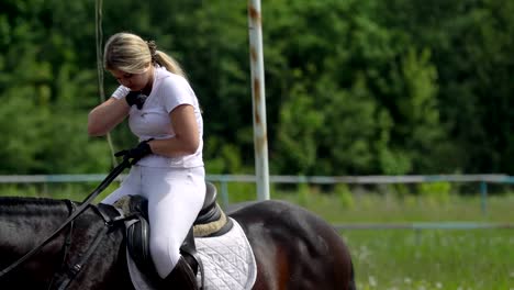 a beautiful girl in white hair and white clothes slowly rides on a black brown stallion. the girl received a message on the smartphone, she pulls out the smartphone and reads the message.