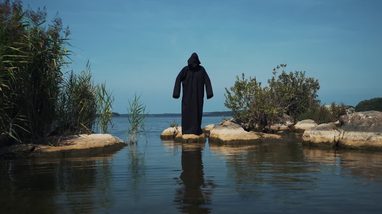 Terrible demon standing in the river. Scary figure in black mantle.