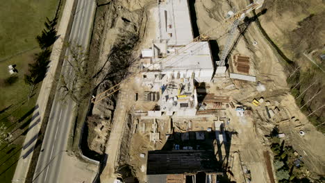 sobrevuelo aéreo del sitio de construcción rural con grúa al lado de la carretera rural con la conducción de automóviles durante el día soleado
