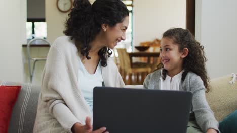 Feliz-Madre-E-Hija-De-Raza-Mixta-Sentadas-En-El-Sofá,-Divirtiéndose-Y-Usando-Una-Computadora-Portátil