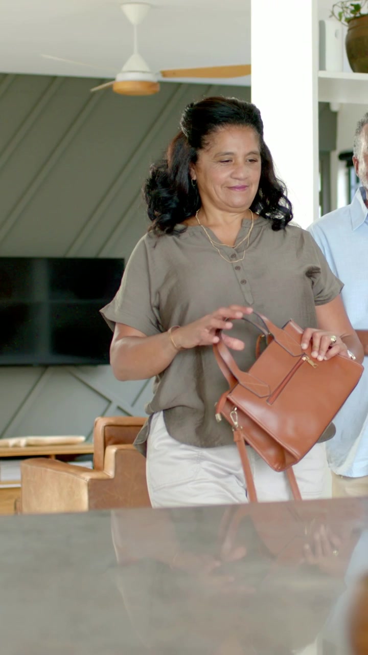 Video verticale: Entrando in casa, donna con blusa color oliva che sistema una borsa di pelle color cuoio per appoggiarla sul bancone.
