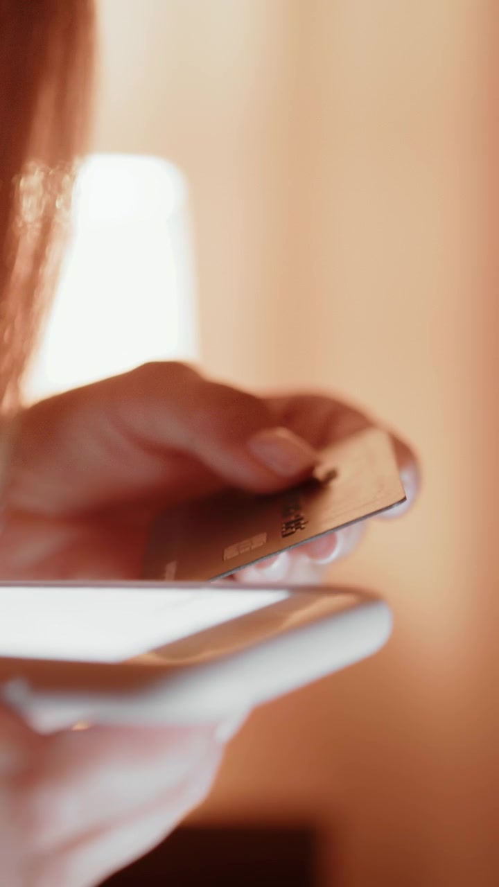 La mano di una persona che tiene una carta di credito sopra uno smartphone, suggerendo acquisti online o transazioni finanziarie.