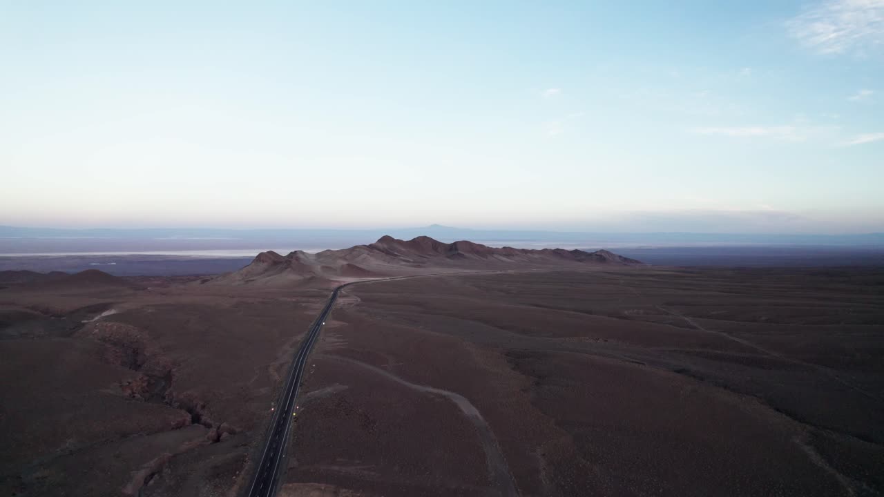 Aerial view of a lonely highway cutting through the arid Atacama Desert, Chile. Vast brown plateau under soft morning light and a pale blue sky