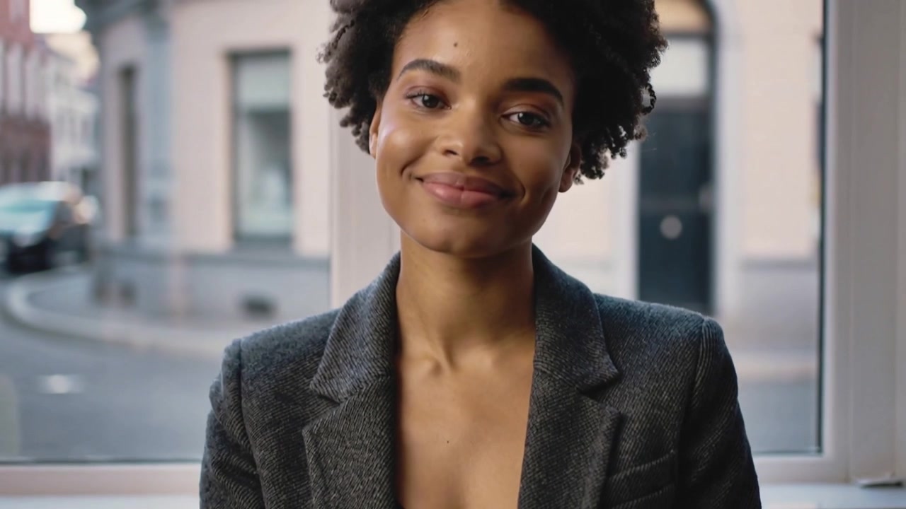 Donna in blazer grigio scuro che fa scivolare una tessera bianca su un tavolo di vetro, sorridendo per condividere i contatti
