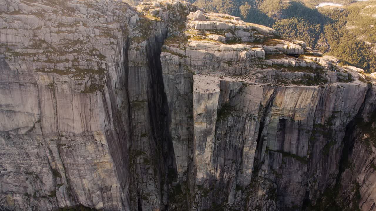 Cinematic drone shot over Norway's Preikestolen cliff with hikers at Lysefjord on a bright day.