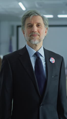 Portrait-of-businessman,-United-States-of-America-elections-voter.-Mature-man-stands-in-a-modern-polling-station,-poses-and-looks-at-camera,-smiles.-Background-with-voting-booths.-Civic-duty-concept.