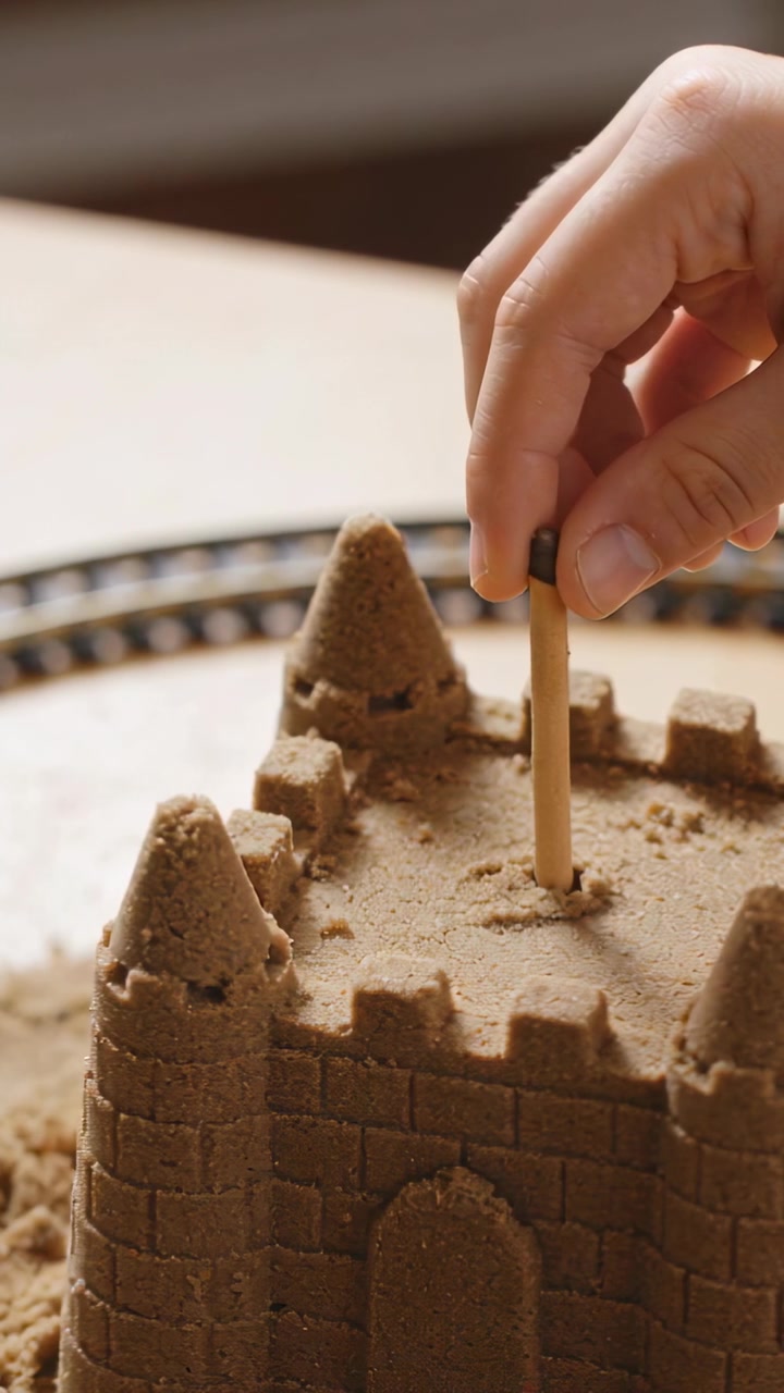 Vertical video: Entering hand pressing biscuit stick into sandcastle on tray, adding chocolate tip