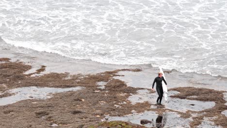 surfer carrying board on rocky beach