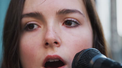 primer plano de una músico femenina cantando en el micrófono al aire libre en la calle