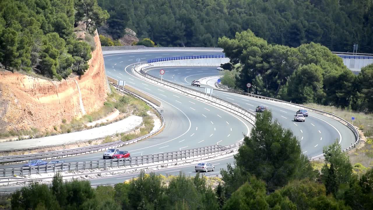 주변에 푸른 나무가 있는 구불구불한 고속도로를 달리는 자동차