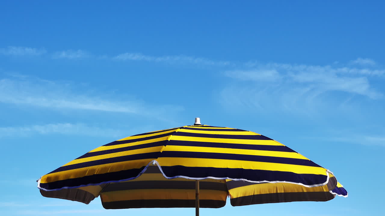 Yellow and navy striped beach umbrella with the blue sky on the background