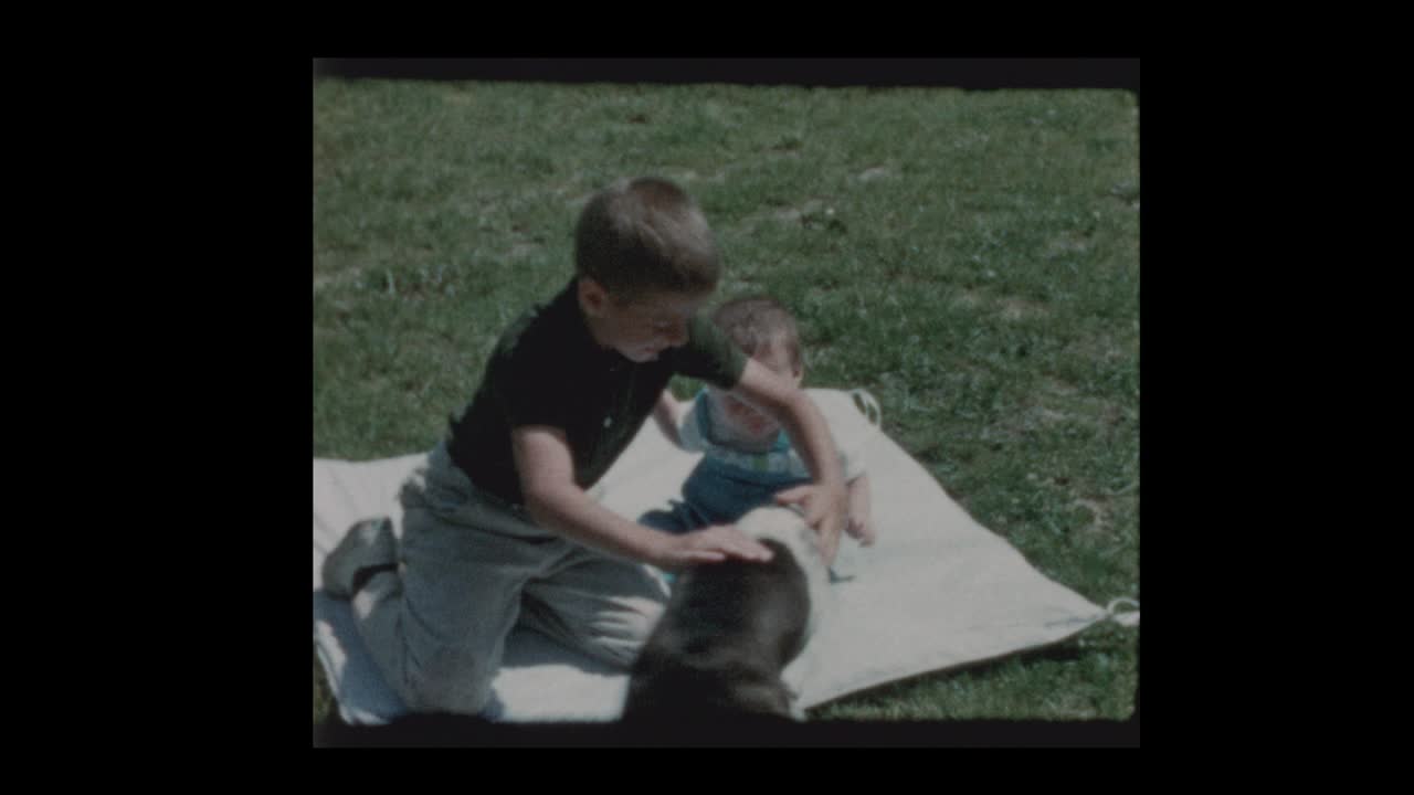 어린 소년과 아기 형제는 마당에서 담요에 개와 함께 놀고 있습니다.