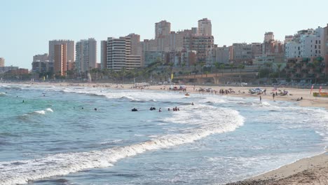 sunbathers and beachgoers bask in the mediterranean warmth at el campello, costa blanca, alicante, with swimmers enjoying the shallow waters near the shoreline in spain