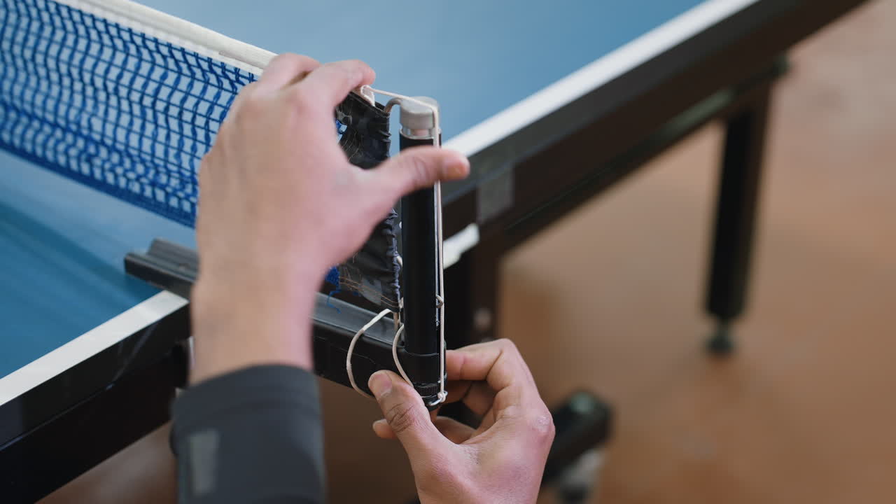 Close up of athlete tightening table tennis net indoors, ensuring proper setup and alignment before competitive game, showing discipline, focus, and preparation for sports performance