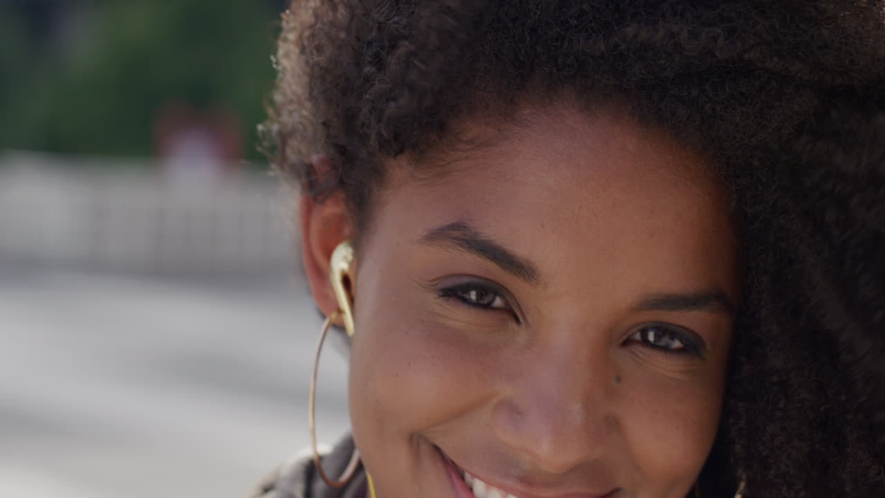 Ritratto di felice donna afroamericana sorridente che indossa le cuffie in uno scenario urbano