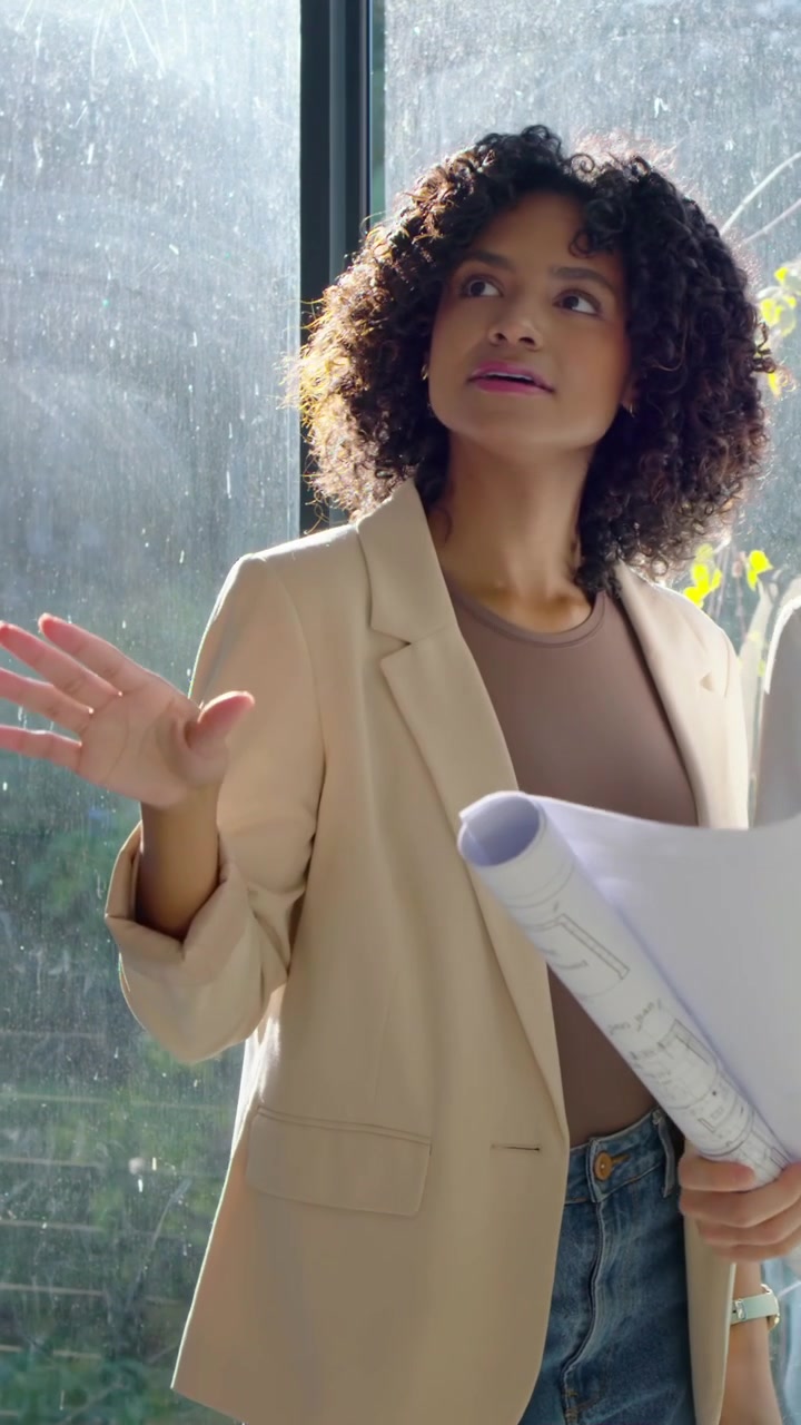 Video verticale: Donna in blazer che indica, con in mano dei progetti, gesticolando vicino alla finestra per la revisione