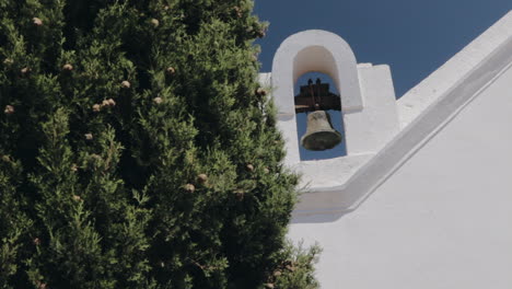 White-Spanish-Catholic-Church-Bell-and-Cross-with-blue-sky-background-covered-by-pine-tree