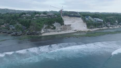 Drone-of-overdevelopment-cliff-collapse-in-Bingin-Beach,-Bali,-Uluwatu-Indonesia-at-golden-hour-sunset-with-low-tide-reef