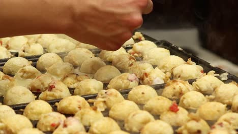 close-up of hands skillfully flipping takoyaki balls on a hot griddle using chopsticks.