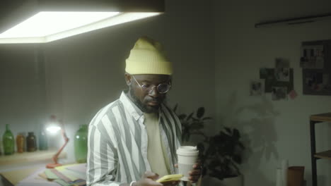 man in beanie and glasses using smartphone with a coffee cup