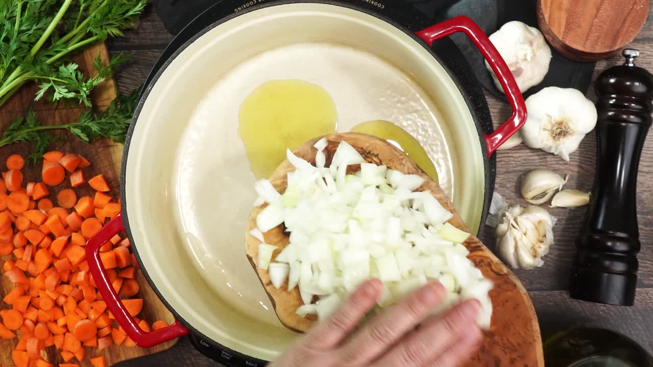 Cooking in olive oil yellow or white onions diced and sliced and in a red stock pot. Sizzling fresh vegetable while cooking Italian Wedding Soup. Using a wooden spoon to mix onions while they sauté.