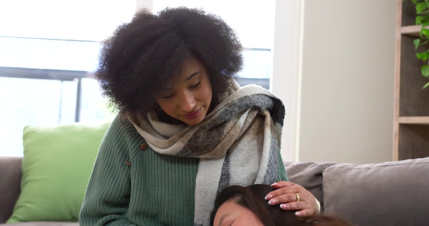 Dopo segnali di disagio, donne diverse su un divano, una che appoggia la testa in grembo all'altra, l'altra che le accarezza i capelli, consolando