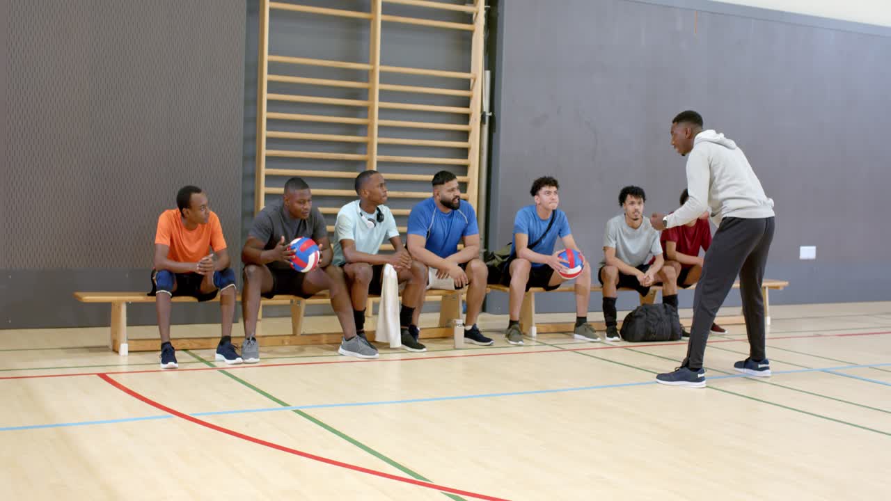 Afroamerikanischer männlicher Trainer trainiert beim Betreten der Turnhalle sein Team mit Volleybällen.