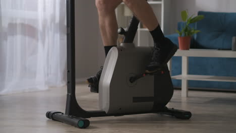 sport a casa durante l'auto-isolamento gambe maschili stanno girando pedali di bicicletta stazionaria in salotto vista ravvicinata allenamento a casa stile di vita sano