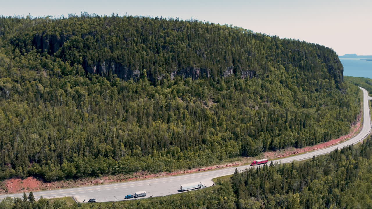 Aerial View of Trucks Driving on a Winding Highway Through a Lush Forest