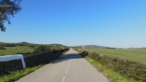 Muñeca-Aérea-A-Lo-Largo-De-Una-Tranquila-Carretera-Al-Aire-Libre-En-El-Lado-Rural-De-Menorca-De-España,-Día-Azul-Claro