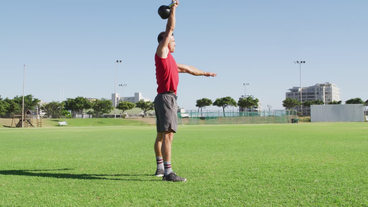 hombre caucásico en forma haciendo ejercicio al aire libre, en cuclillas y levantando pesas de kettlebell con un brazo