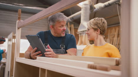 aprendiz femenina aprendiendo de un carpintero adulto con una tableta digital en un taller de muebles