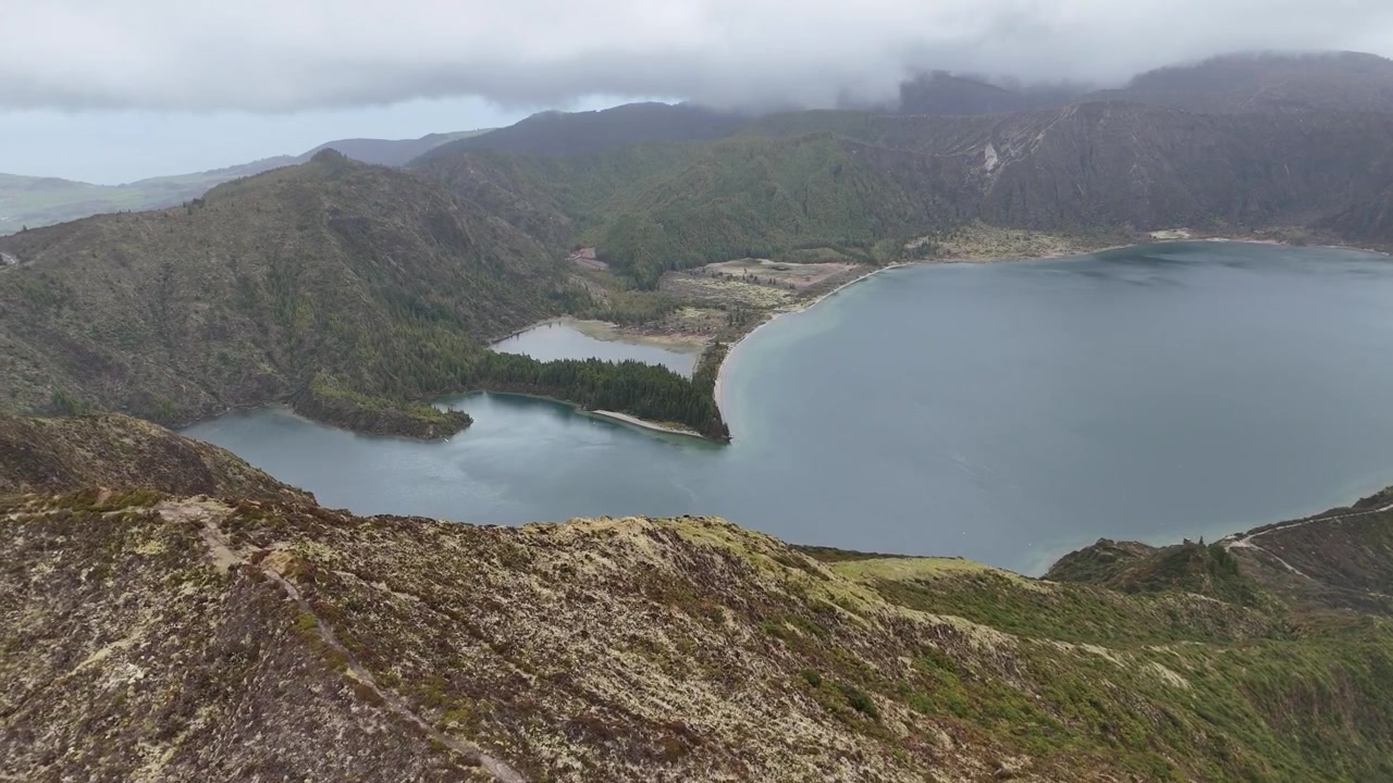 Azorlar, Sao Miguel Adası'ndaki Lagoa do Fogo'ya bakan vahşi dağ sırtları üzerinde havadan drone uçuşu. Yemyeşil yamaçlar ve masmavi krater gölü ile dramatik volkanik manzara.