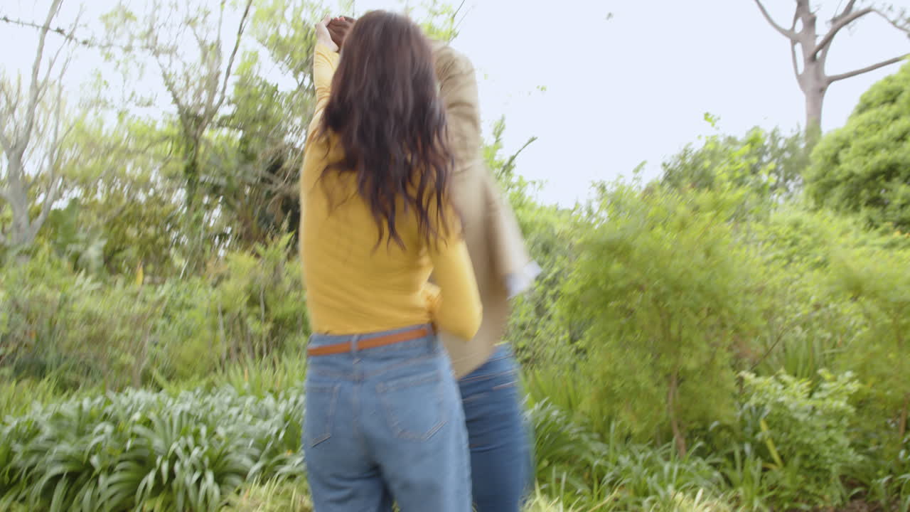 Playfully dancing together, multiracial couple in lush green garden, enjoying nature
