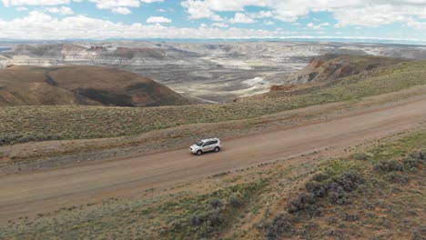 Aerial-pullback-wide-following-car-on-dirt-road-at-Pilot-Butte-Wild-Horse-Scenic-Loop,-Wyoming-USA