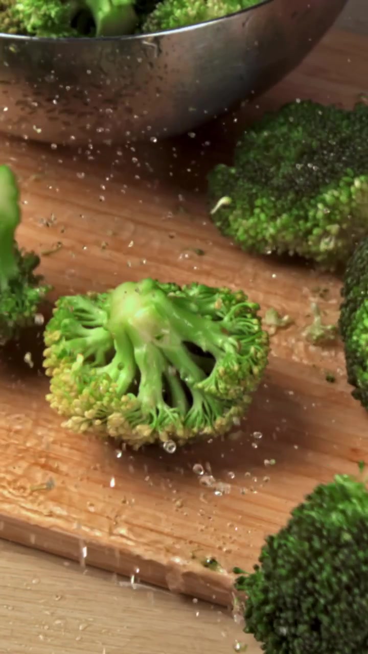 Cimette di broccoli freschi che cadono su un tagliere di legno con schizzi d'acqua