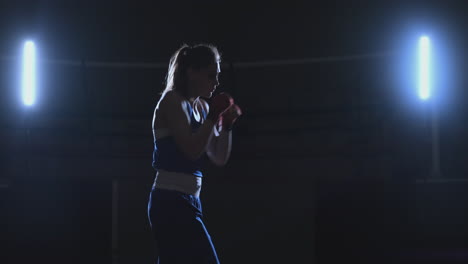 training a beautiful female boxer doing punches in a dark room. steadicam shot. preparation for self-defense and fight in the ring