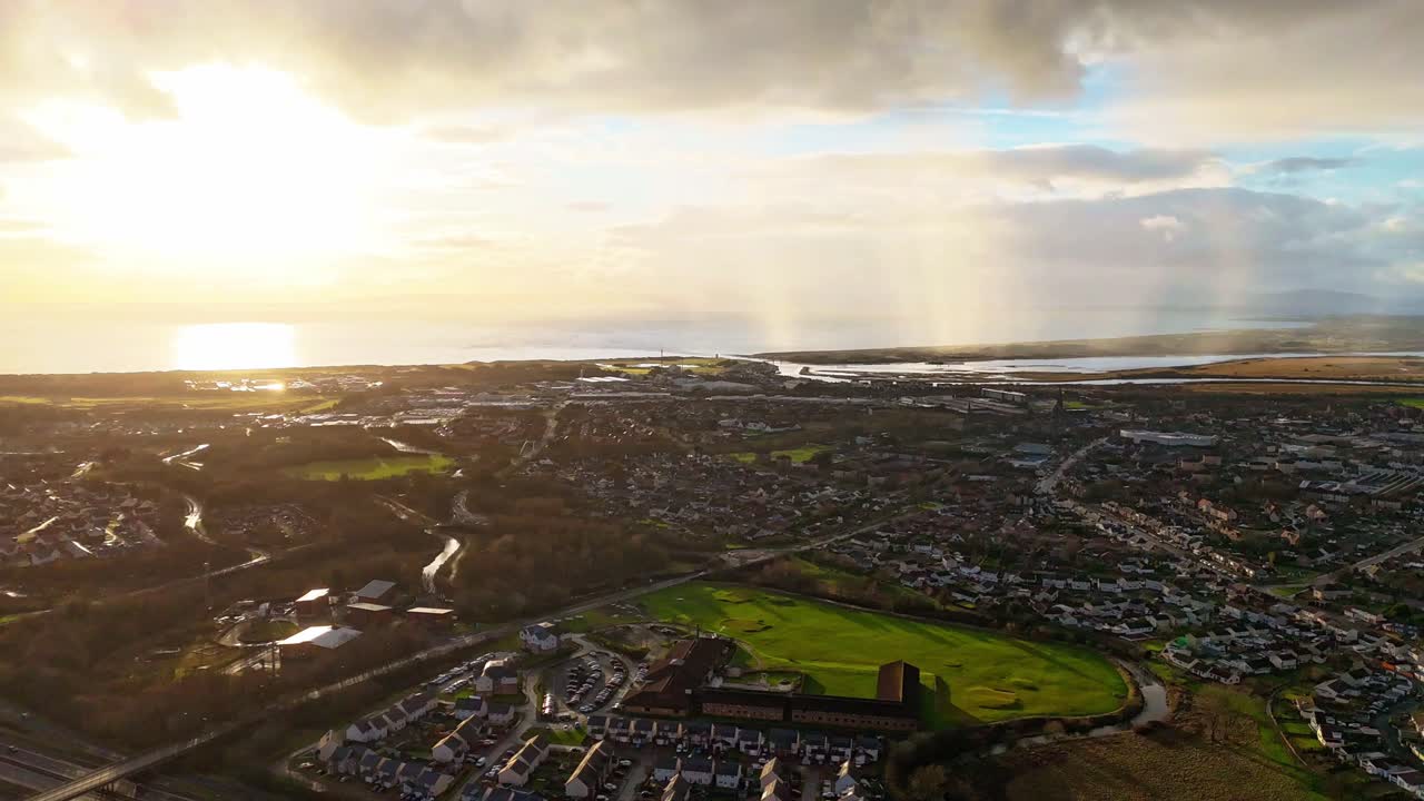 Stunning aerial Timelapse view of a coastal town at sunset with dramatic clouds and scattered rain showers. Warm light reflects off the sea, capturing a peaceful and cinematic landscape