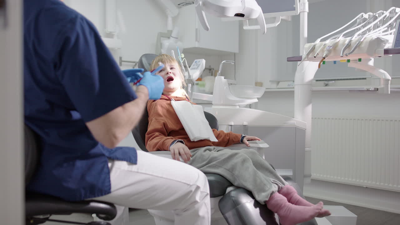 Friendly male dentist talks to smiling gap-toothed boy in chair after oral exam