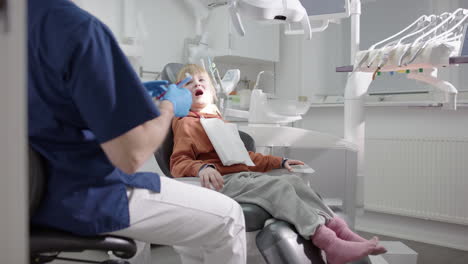 friendly male dentist talks to smiling gap-toothed boy in chair after oral exam
