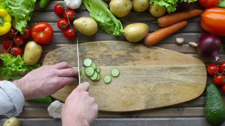 Man Slicing Cucumber with Knife on Wooden Cutting Board