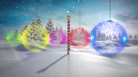 colorful bauble decorations hanging against snow falling over north pole on winter landscape