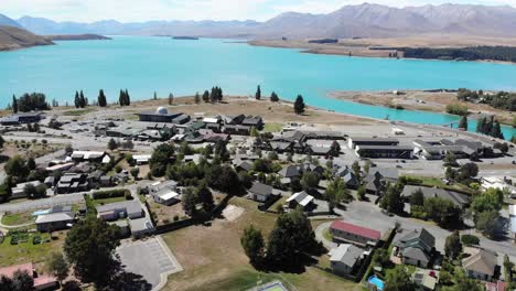 Aerial-view-of-small-town-on-turquoise-Lake-Tekapo-lakefront,-main-street-and-observatory