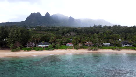 zoom aéreo en la casa de la playa de kauai en un día nublado con siluetas de montañas en el fondo